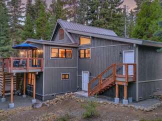 Experience mountain living in this stunning modern home, featuring a spacious elevated deck perfect for outdoor entertaining and enjoying the serene forest surroundings.