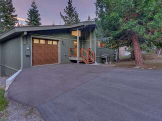 Nestled among tall trees, this charming home features a rustic wooden garage door and a welcoming entrance with wooden stairs and railings.
