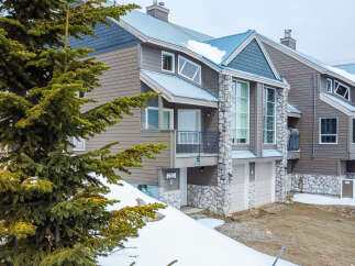 Experience luxury mountain living in this stunning townhouse featuring a modern exterior with stone accents and a sleek metal roof.