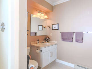 This charming bathroom features a clean white vanity with a cultured marble countertop, complemented by a large mirror and a stylish vanity light fixture.