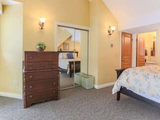 This charming bedroom features a spacious bed with a light-colored botanical print comforter, complemented by a dark wood dresser and mirrored closet doors.