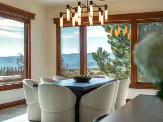 Experience breathtaking mountain views from this elegant dining room, featuring a modern chandelier and comfortable upholstered chairs.