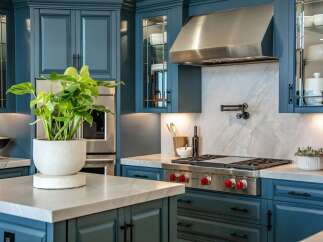 Experience luxury in this stunning kitchen featuring deep teal cabinetry and a sleek stainless steel range hood.
