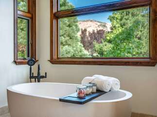 Indulge in ultimate relaxation in this luxurious bathroom, featuring a stunning freestanding bathtub with a view of the picturesque mountains and lush greenery.