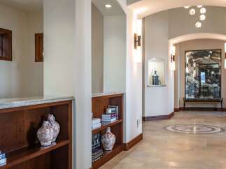 This elegant hallway features built-in wooden bookshelves displaying decorative vases and books, complemented by sophisticated wall sconces and recessed lighting.