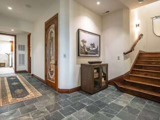Step into this elegant entryway featuring a beautiful wooden staircase and a decorative rug on slate tile flooring.