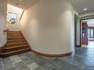 This spacious entryway features a grand wooden staircase leading to the upper level, complemented by elegant slate tile flooring.
