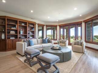 Experience luxury living in this spacious living room, featuring a custom built-in bookshelf and large windows that offer stunning views of the outdoors.