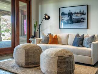 Experience sophisticated living in this elegant living room, featuring a plush sofa adorned with decorative pillows and two stylish poufs.