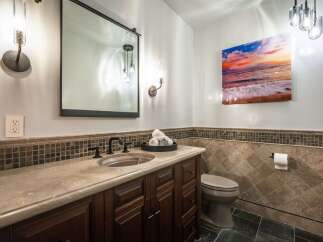 This elegant bathroom features a dark wood vanity with a stone countertop and a vessel sink, complemented by a large framed mirror and modern sconce lighting.