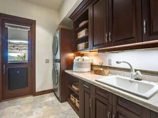 Discover this beautifully appointed laundry room featuring a stacked washer and dryer, ample dark wood cabinetry for storage, and a spacious sink area.