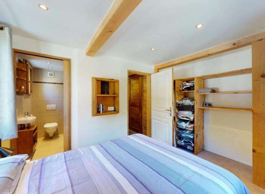 Discover this charming bedroom featuring a comfortable bed with striped linens and a convenient en-suite bathroom.