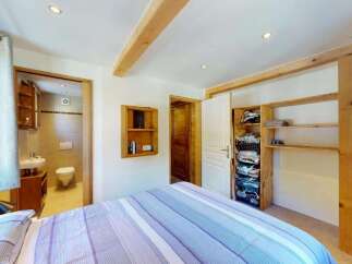 Discover this charming bedroom featuring a comfortable bed with striped linens and a convenient en-suite bathroom.
