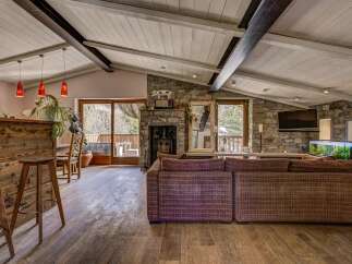 Experience rustic charm in this spacious living area, featuring a cozy stone fireplace and a vaulted wood-paneled ceiling with exposed beams.