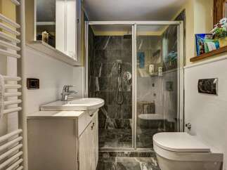 This charming bathroom features a sleek glass-enclosed shower with dark, modern tilework.