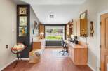 This home office features a spacious built-in desk with ample storage and a large window overlooking a lush green yard.