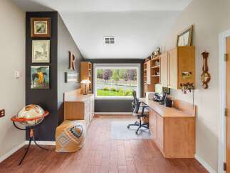 This home office features a spacious built-in desk with ample storage and a large window overlooking a lush green yard.