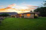 Experience serene living in this charming home, nestled against a majestic mountain backdrop under a vibrant sunset sky.