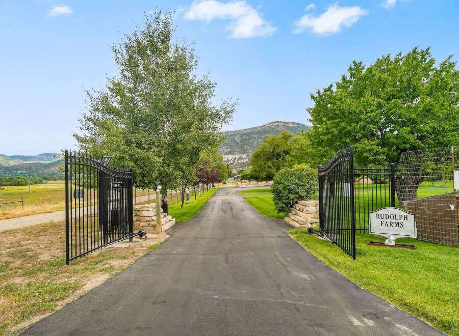 Welcome to Rudolph Farms, a stunning property offering a picturesque setting with a long, paved driveway leading through elegant black gates.