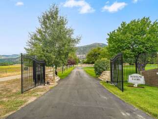 Welcome to Rudolph Farms, a stunning property offering a picturesque setting with a long, paved driveway leading through elegant black gates.
