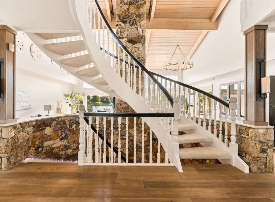 Experience luxury living with this stunning spiral staircase, featuring a natural stone accent wall and elegant white balusters.