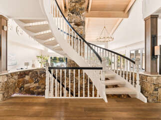 Experience luxury living with this stunning spiral staircase, featuring a natural stone accent wall and elegant white balusters.