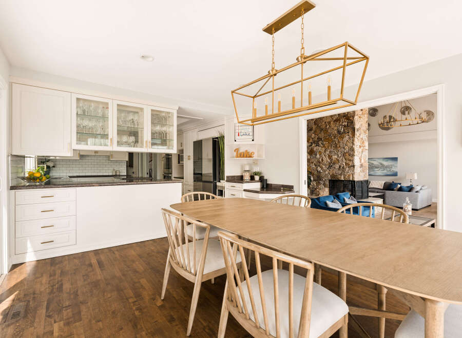 This spacious dining area seamlessly connects to a modern kitchen, featuring elegant white cabinetry and glass-front display shelves.