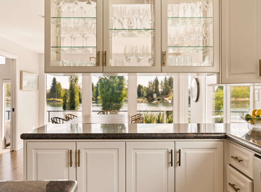 Experience breathtaking lake views from this stunning kitchen, featuring elegant glass-front cabinetry filled with glassware.