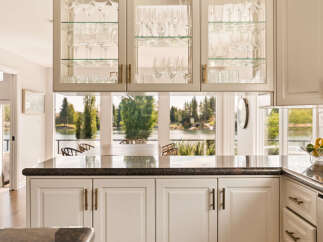 Experience breathtaking lake views from this stunning kitchen, featuring elegant glass-front cabinetry filled with glassware.