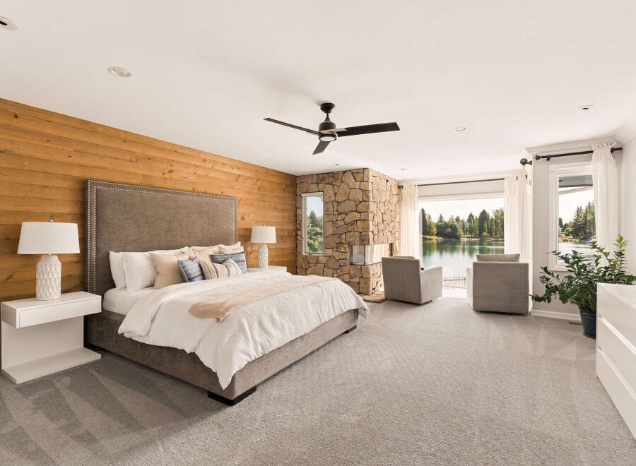 Experience luxury living in this stunning master suite, featuring a king-sized bed with a tufted headboard and a cozy reading nook by the stone fireplace.