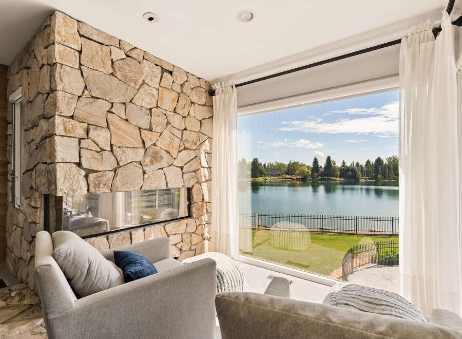 Experience breathtaking lake views from this stunning living room, featuring a dramatic floor-to-ceiling stone fireplace.