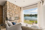 Experience breathtaking lake views from this stunning living room, featuring a dramatic floor-to-ceiling stone fireplace.