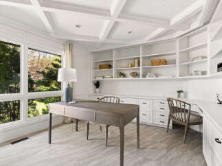 This home office features a coffered ceiling and expansive windows that flood the space with natural light.