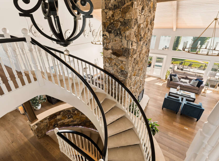 Experience luxury living in this stunning home featuring a grand spiral staircase with a stone accent wall and a dramatic chandelier.