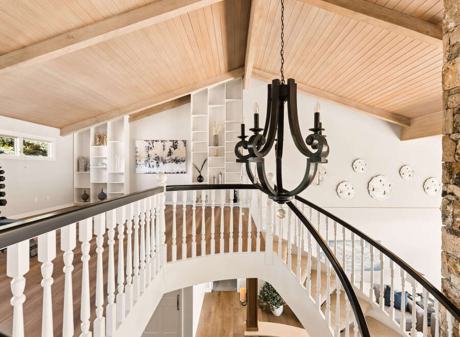 Ascend this grand staircase featuring a dark wrought-iron chandelier and a rustic stone accent wall.