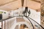 Ascend this grand staircase featuring a dark wrought-iron chandelier and a rustic stone accent wall.