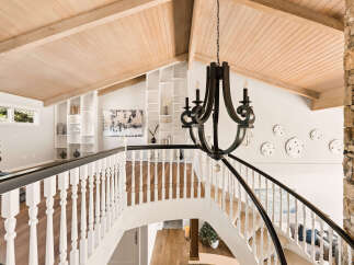 Ascend this grand staircase featuring a dark wrought-iron chandelier and a rustic stone accent wall.