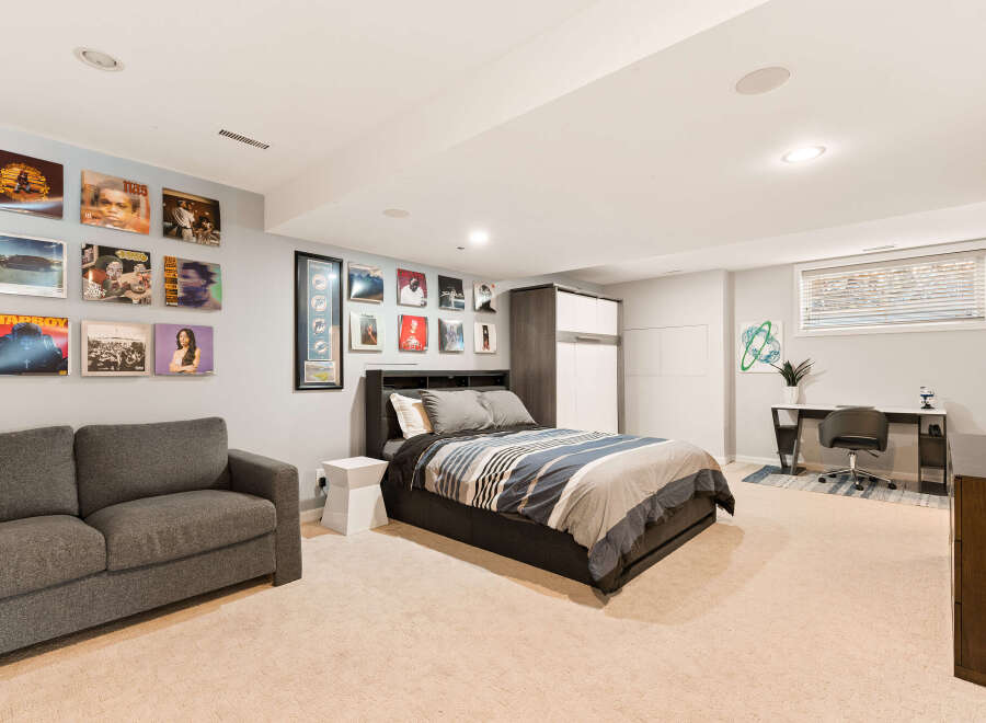 Discover this stylish basement bedroom featuring a comfortable grey sofa and a queen-sized bed with a modern striped comforter.