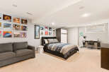 Discover this stylish basement bedroom featuring a comfortable grey sofa and a queen-sized bed with a modern striped comforter.