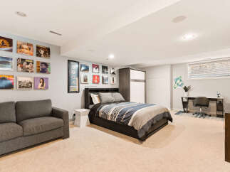 Discover this stylish basement bedroom featuring a comfortable grey sofa and a queen-sized bed with a modern striped comforter.