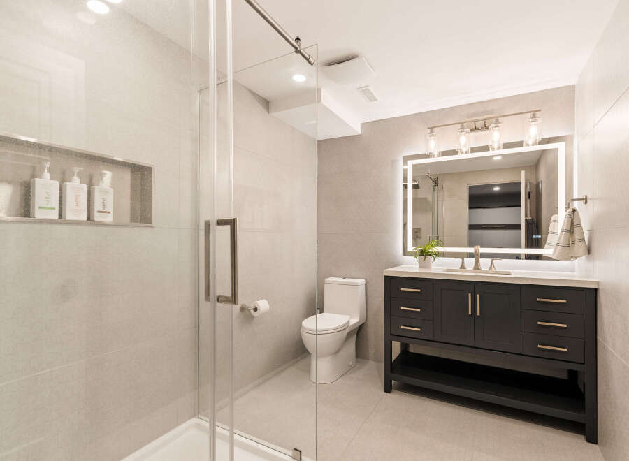 This modern bathroom features a sleek glass-enclosed shower and a stylish dark wood vanity with a quartz countertop.