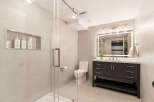 This modern bathroom features a sleek glass-enclosed shower and a stylish dark wood vanity with a quartz countertop.