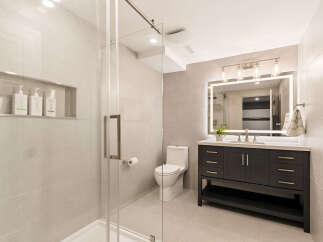This modern bathroom features a sleek glass-enclosed shower and a stylish dark wood vanity with a quartz countertop.