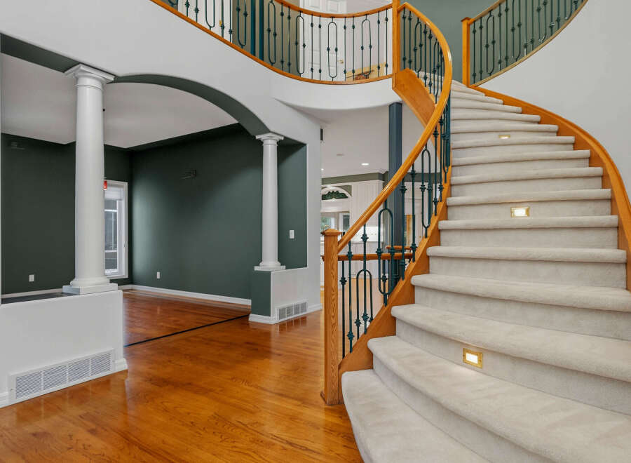 Experience grand living in this stunning home featuring a dramatic curved staircase with plush carpeting and elegant lighting.