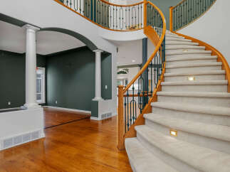 Experience grand living in this stunning home featuring a dramatic curved staircase with plush carpeting and elegant lighting.
