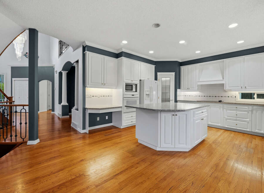 Step into this spacious and elegant kitchen, featuring pristine white cabinetry, a large granite-topped island, and a built-in desk area perfect for quick tasks.
