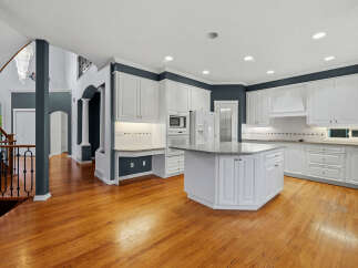 Step into this spacious and elegant kitchen, featuring pristine white cabinetry, a large granite-topped island, and a built-in desk area perfect for quick tasks.