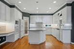 This spacious kitchen boasts pristine white cabinetry, complemented by a large central island with a granite countertop, perfect for meal preparation and casual dining.