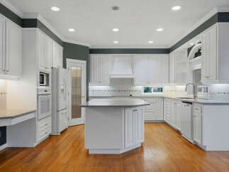 This spacious kitchen boasts pristine white cabinetry, complemented by a large central island with a granite countertop, perfect for meal preparation and casual dining.