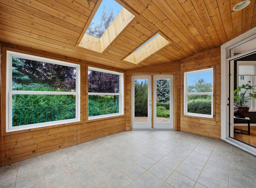 Experience seamless indoor-outdoor living in this charming sunroom, featuring a warm wood-paneled interior and a vaulted ceiling with skylights.